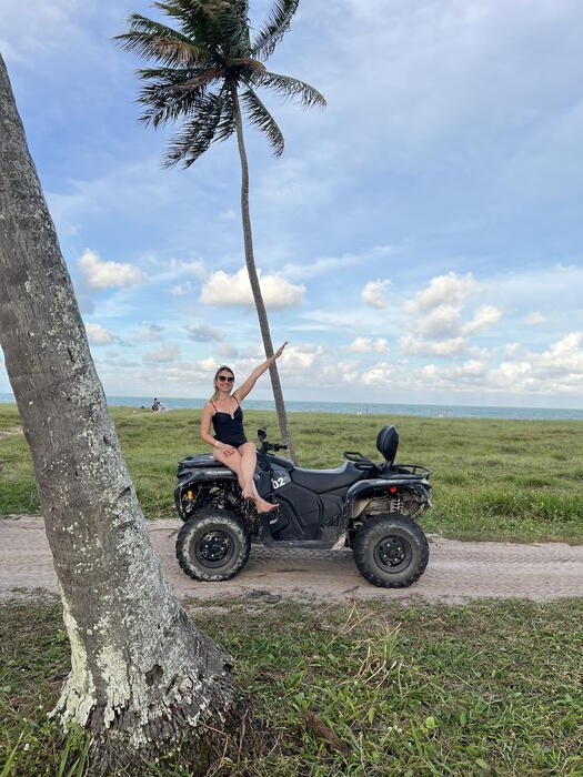 Mulher em cima de um quadriciclo perto de coqueiro na praia